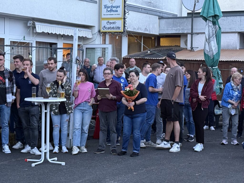 Eine Gruppe von Menschen vor der Gaststätte. In der Mitte die Familie Farmakis mit Blumenstrauß.
