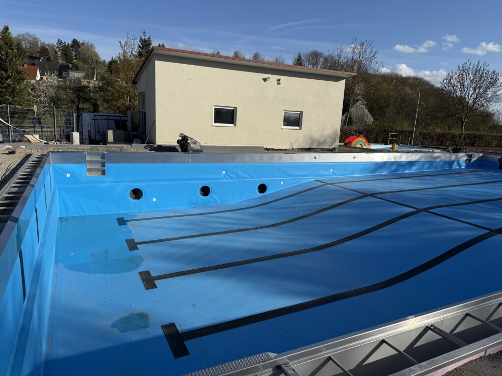 Technikgebäude des Schwimmbades und leeres Schwimmbecken mit blauer Folie.